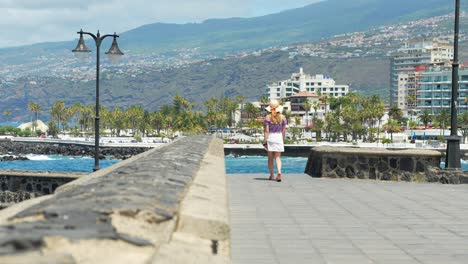 Mujer-Caucásica-Caminando-Por-El-Hermoso-Paseo-Marítimo,-Centros-Turísticos-En-Segundo-Plano.