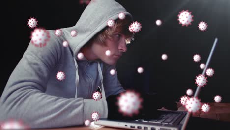 animation of of macro covid19 cells over man wearing hoodie, using a laptop