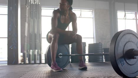 resting on barbell, woman in gym taking break from weightlifting workout