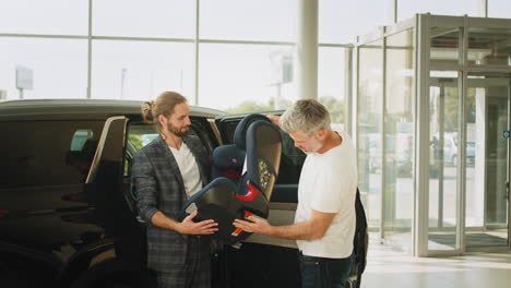 men inspecting a child car seat in a car showroom