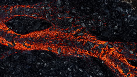 Red-hot-lava-flow-streaming-over-black-volcanic-rocks,-aerial-directly-above