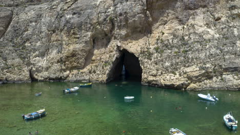 Cueva-De-Dwerja-Y-Una-Bahía-Marina-Con-Una-Ciudad-Portuaria-Con-Barcos,-Malta,-Antena