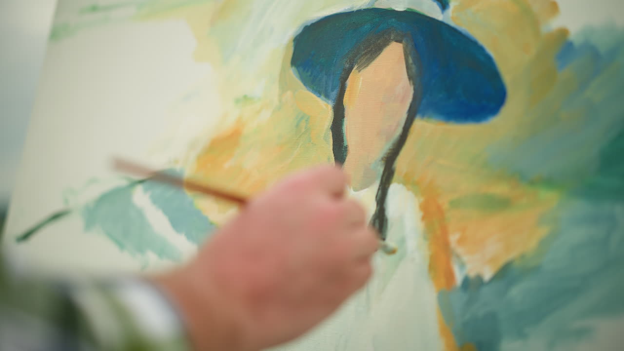 se ve la mano de un artesano, vestido con una camisa a cuadros, sosteniendo un pincel mientras pinta hábilmente y suavemente un retrato vibrante en un lienzo