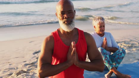 Senior-african-american-couple-practising-yoga-at-the-beach