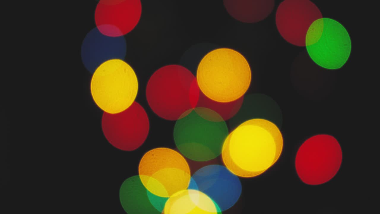 Multicolored light leaks footage on black background. Festival decorative string lights hang and glow outdoors at night. Decoration for holiday. Natural lighting bokeh effect. For compositing over footage, stylizing, video transition
