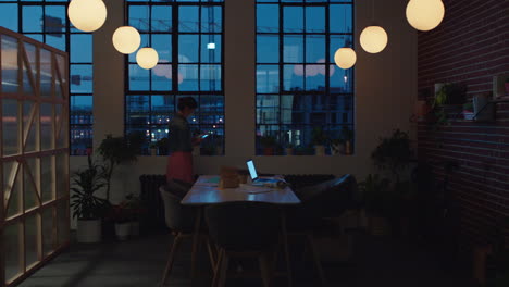 Kaukasische-Geschäftsfrau,-Die-Bis-Spät-In-Die-Nacht-Arbeitet-Und-Ihr-Smartphone-Nutzt,-Um-Ein-Foto-Des-Bauprojektmanagers-Zu-Machen,-Der-Auf-Dem-Laptop-Computer-Surft-Und-Termine-Plant,-Die-Nachts-Im-Büro-Notizen-Schreiben