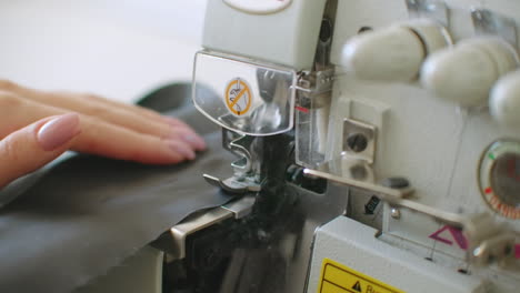 close-up the overstitching machine passes the edges of the black fabric in slow motion. serger process in the sewing workshop