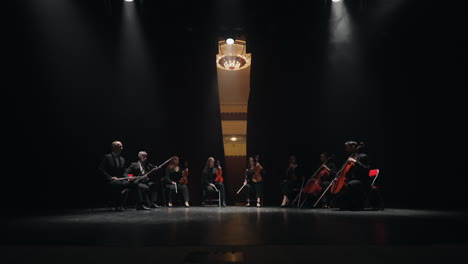 octet of string and wind instrument musicians are sitting on scene of old opera house