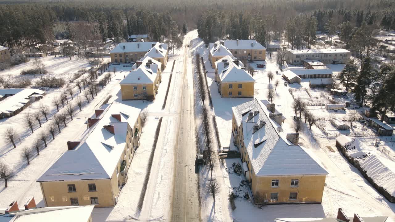 Aerial view of the snow-covered small town of Seda with yellow buildings, streets and roofs covered in white. A peaceful winter landscape in the sunlight.