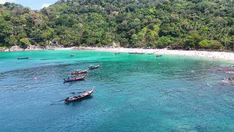 aerial view of a bustling phuket beach with boats, swimmers, and lush greenery under bright sunlight