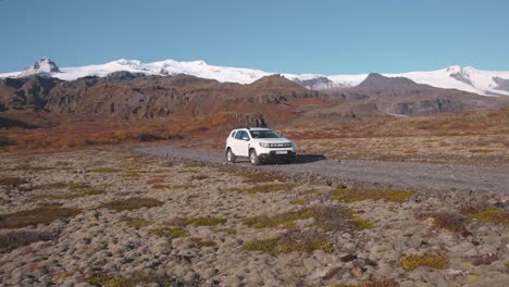 White-car-standing-on-gravel-road-below-snowy-mountains-in-Iceland