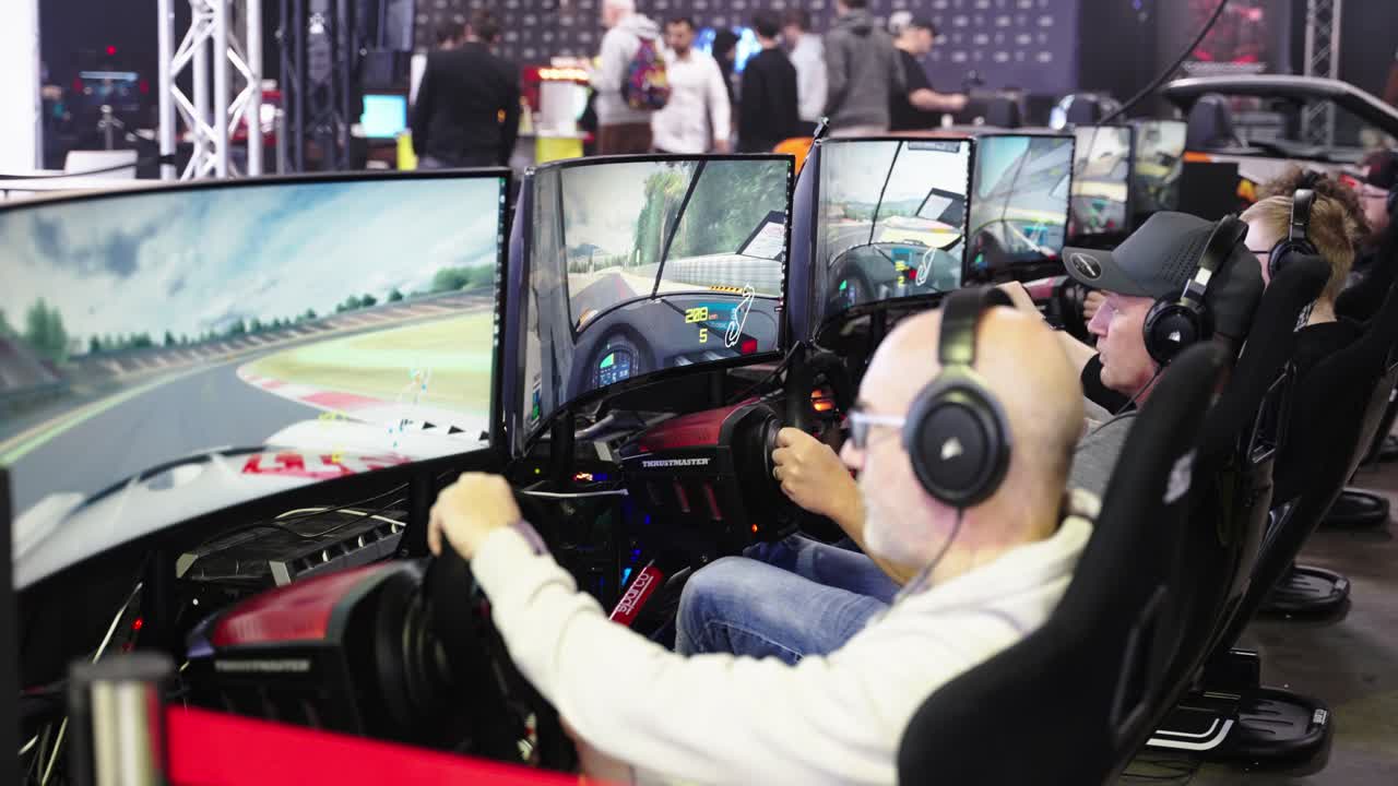 Row of men sitting in front of screens sitting a driver seat with steering wheel and wearing headsets playing a racing game tournament on a convention event at LGX Luxembourg