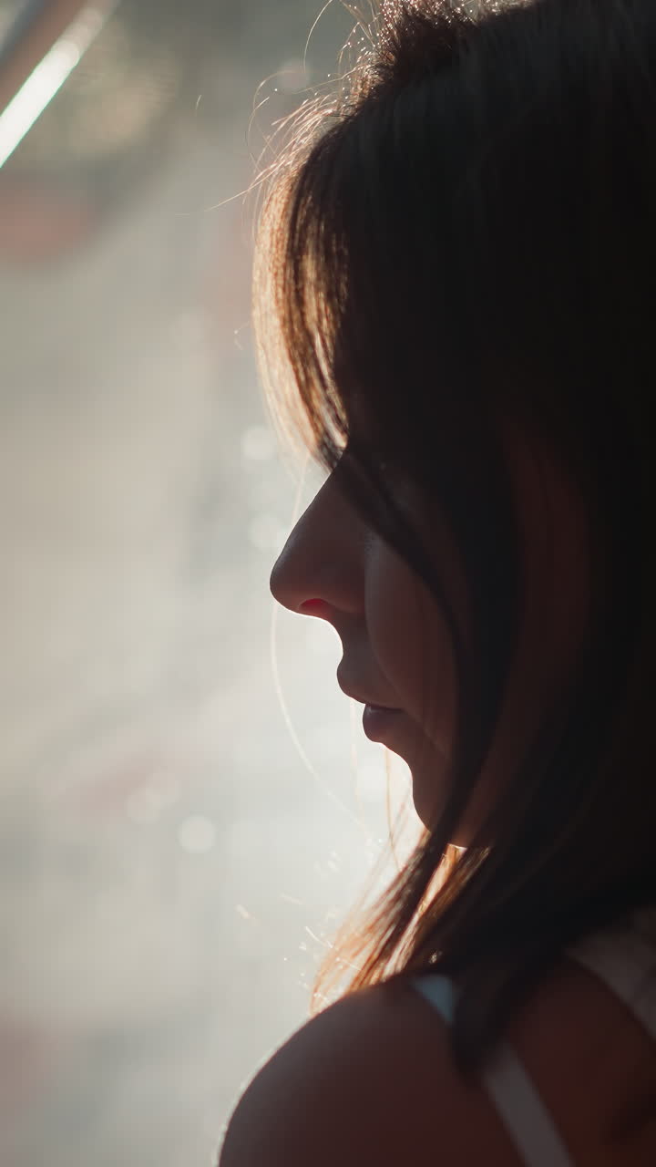 Sad woman silhouette near reflective glass closeup. Lady stands alone by window mirror surface at night. Woman with depression at backlight