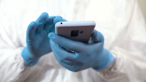 hands of doctor dressed in ppe checking things on mobile phone with finger and gloves on