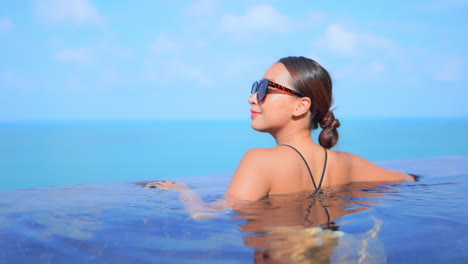 back of attractive woman learning on the edge of infinity pool with stunning view of open seascape on background, - sunny day slow motion