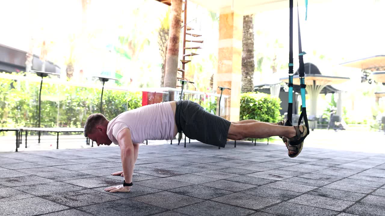 Giovane uomo che fa flessioni con le gambe appese alle TRX