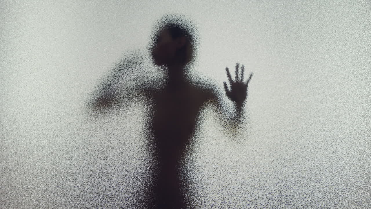 A female silhouette behind the frosted window touches the glass slowly