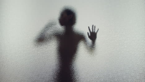 a female silhouette behind the frosted window touches the glass slowly