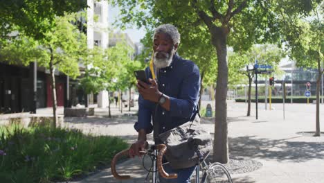 African-american-senior-man-with-bicycle-using-smartphone-on-the-road