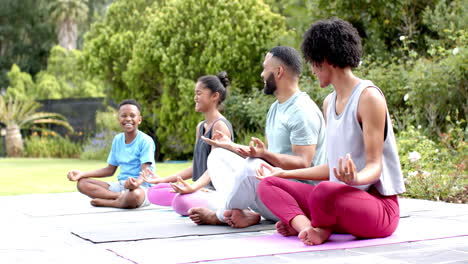 happy african american parents, son and daughter doing yoga meditation in garden, slow motion