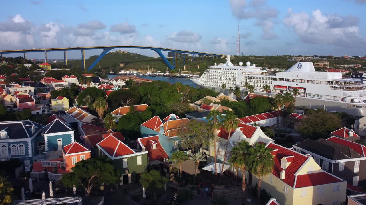 Luftfoto som zoomer inn på Dronning Julianas bro og et lite cruiseskip som krysser kolonibygninger