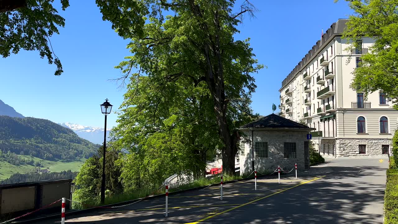 Panoramic wide shot of Bürgenstock Hotel in Lucerne during sunny day. Lucerne Lake with blue sky and snowy mountains in background, Switzerland. Panning shot.
