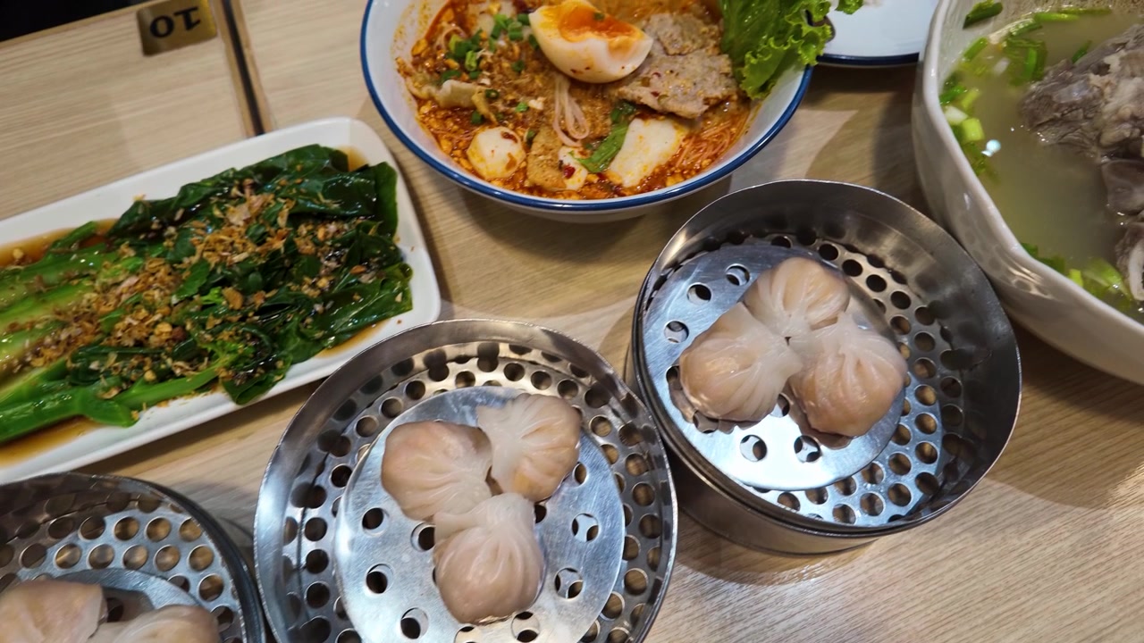 Pengambilan gambar panning sudut tinggi dim sum, bok choy, dan sup mi di meja restoran
