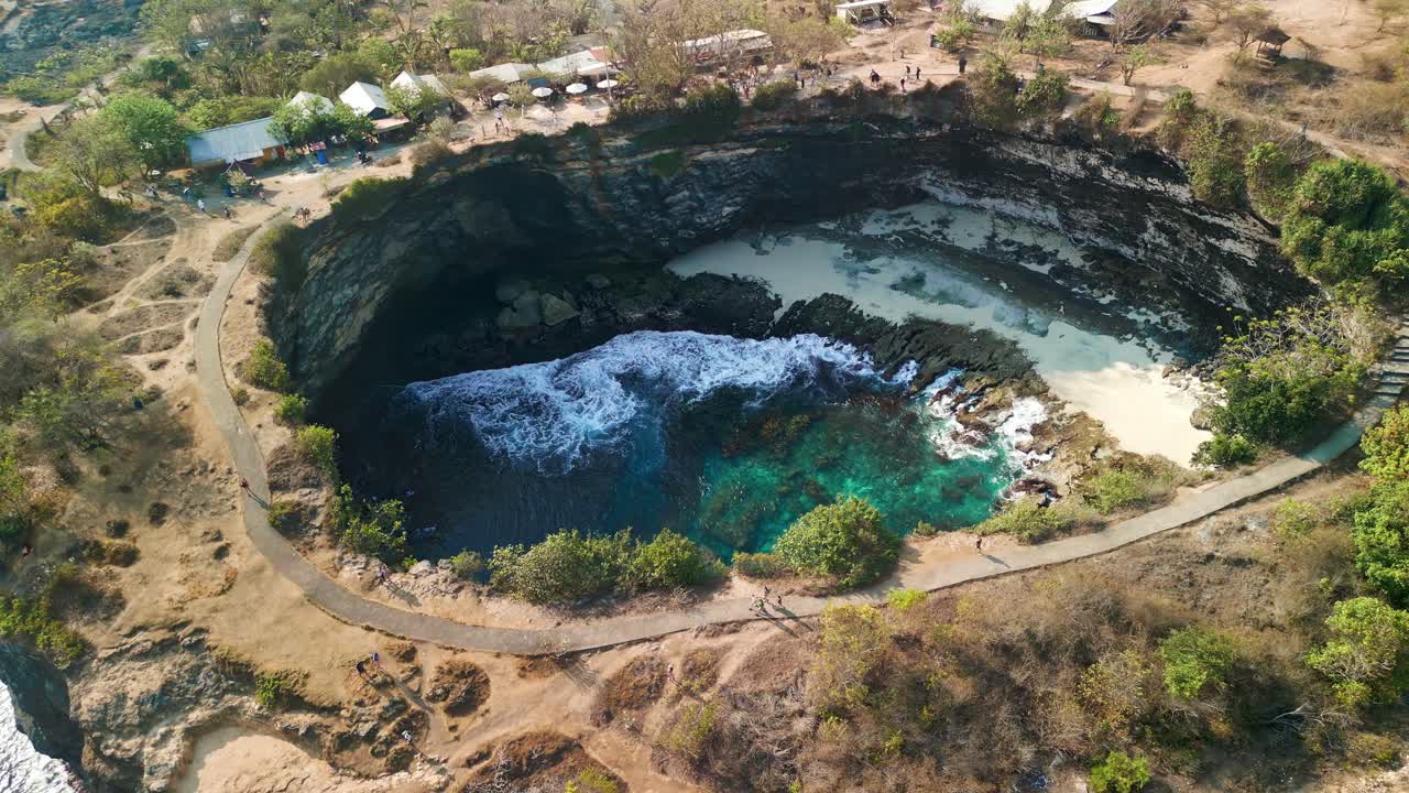 Orbit aerial view of a collapsed cave filled with sea water and a beach (Broken Beach, Nusa Penida)