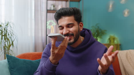 Happy-excited-indian-man-making-phone-conversation-talking-with-friend-sitting-call-on-couch-at-home