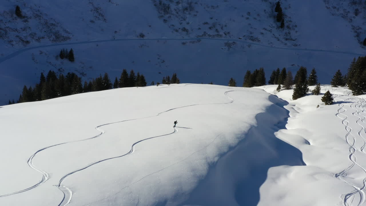 toma aérea rastreando a un snowboarder fuera de pista, con nieve fresca y sol a lo largo de una cresta nevada en los alpes franceses en invierno