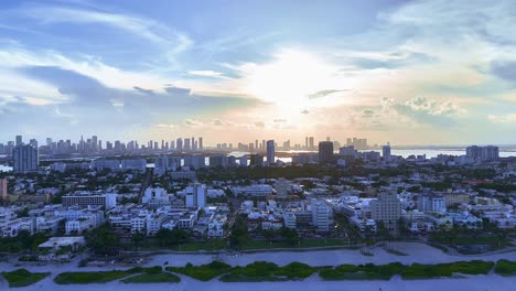 un dron vuela hacia atrás desde south beach a última hora de la tarde, capturando la puesta de sol, ocean avenue, la playa, la costa, el océano y los horizontes de la playa de miami y el centro de miami.