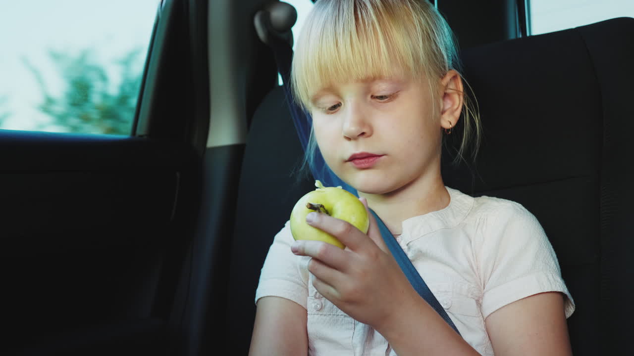 Spuntino in viaggio: la bambina mangia una mela sul sedile posteriore dell'auto. Video 4k.