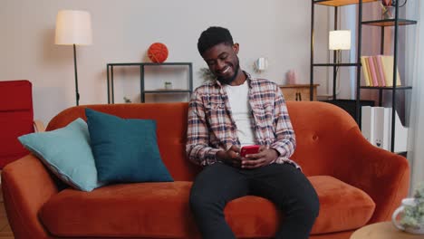 cheerful young man sitting on sofa using mobile phone share messages on social media application