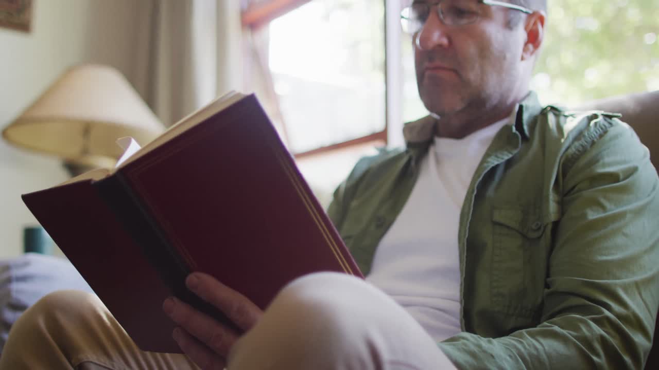 hombre caucásico sentado en el sofá, leyendo un libro en casa