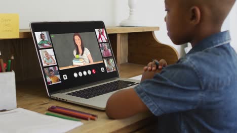 Schoolboy-using-laptop-for-online-lesson-at-home,-with-diverse-teacher-and-class-on-screen