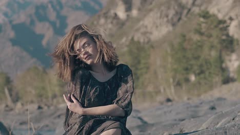 una mujer soñadora con un vestido suelto se sienta en una piedra en un día ventoso