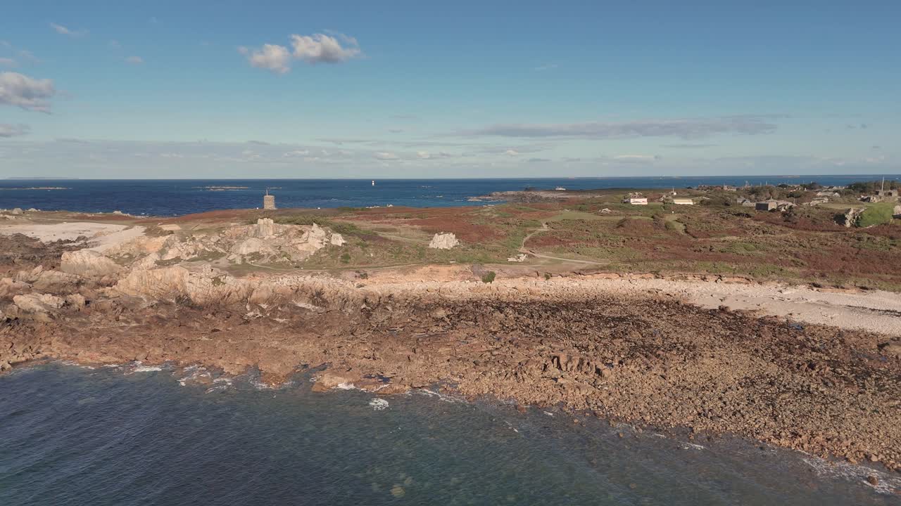 Lancresse Bay Guernsey panning over shoreline of beach with rocky outcrops on sunny day with calm lapping waves showing Martello Tower and Fort Le Marchant