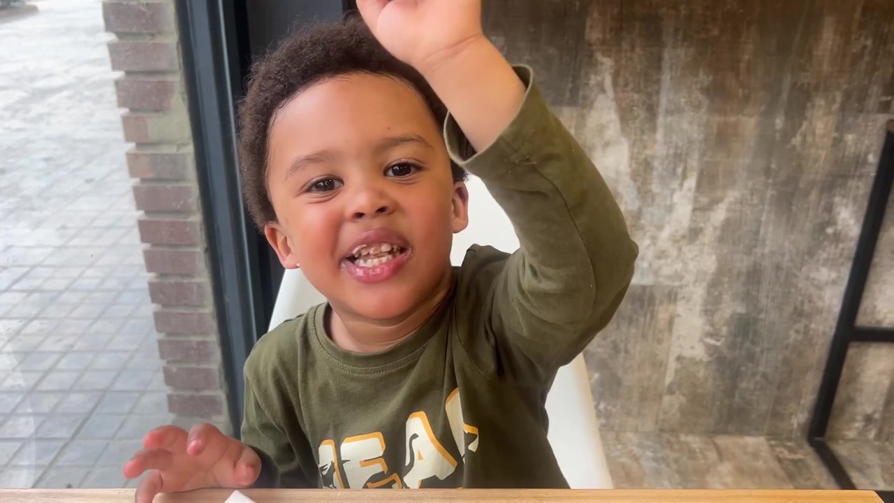Bambino di colore di tre anni carino si pulisce le mani con un tovagliolo dopo aver mangiato cioccolato seduto all'interno di una caffetteria