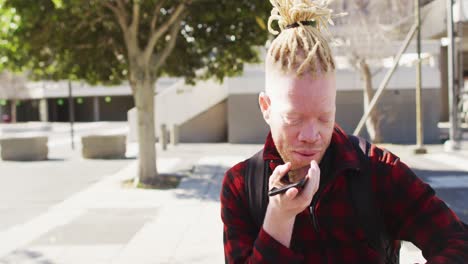 Happy-albino-african-american-man-with-dreadlocks-in-park-talking-on-smartphone