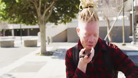feliz albino hombre afroamericano con rastas en el parque hablando en el teléfono inteligente