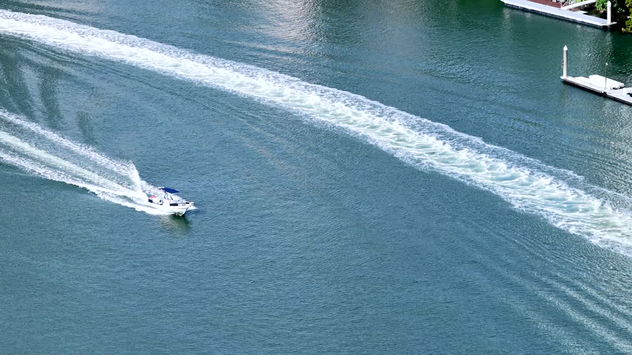 Aerial view of speedboat creating wake on calm waterway, bright daylight, smooth camera tracking