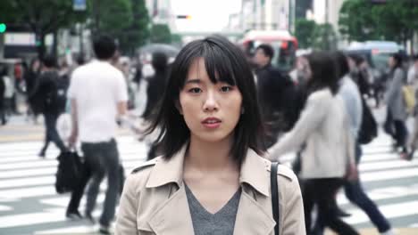 a young woman stands still amidst a crowded crosswalk in tokyo, surrounded by hurried pedestrians. the urban setting is vibrant, filled with movement and city life.