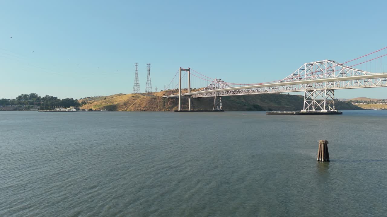 The Alfred Zampa Memorial Bridge extends across the Carquinez Strait like a ribbon of steel, viewed from a dynamic aerial shot near Crockett’s port