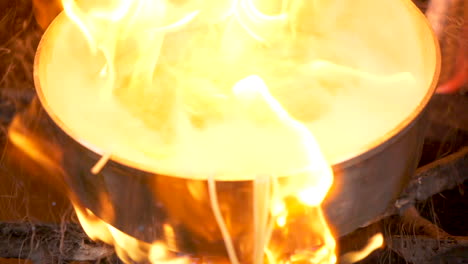 a close up shot of a pan on fire with flambe pasta in slow motion