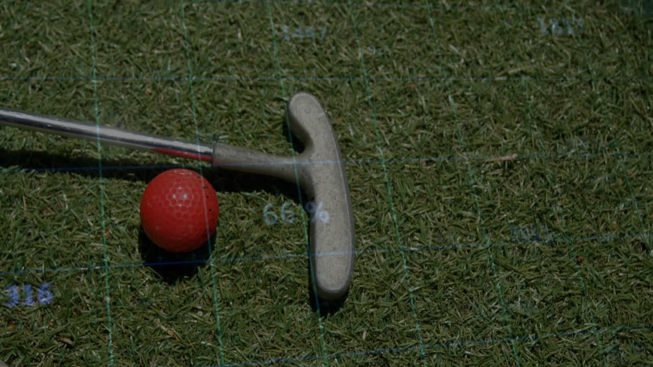 Red golf ball being positioned next to golf putter head on grass, showing digital grid overlay