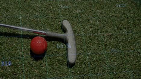 red golf ball being positioned next to golf putter head on grass, showing digital grid overlay