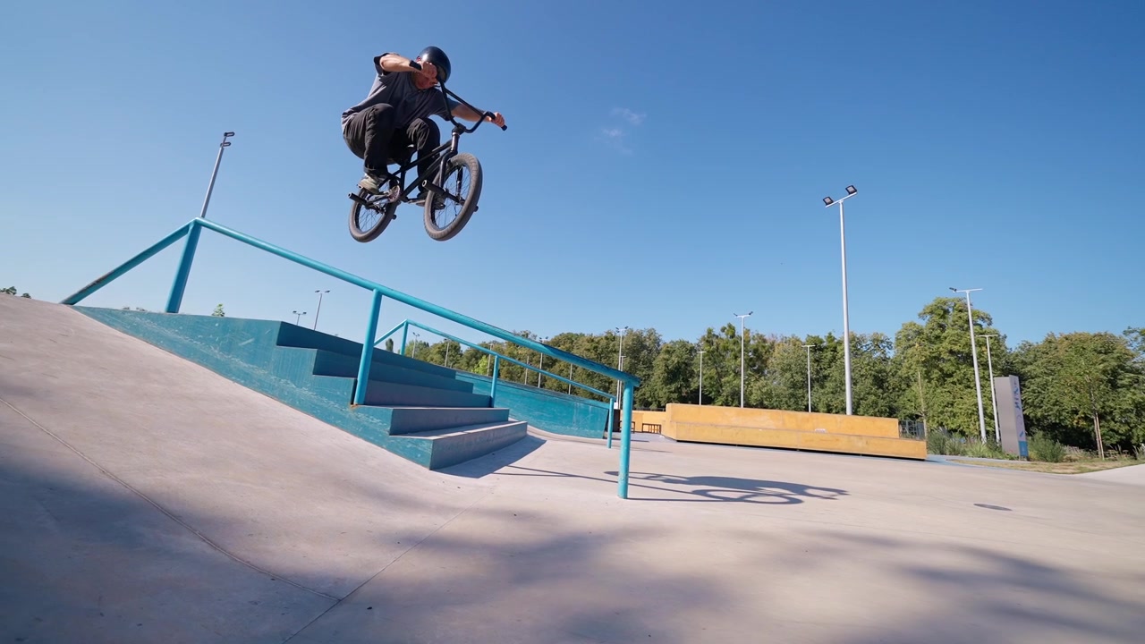 Giovane uomo in BMX salta sopra un rail in uno skatepark.