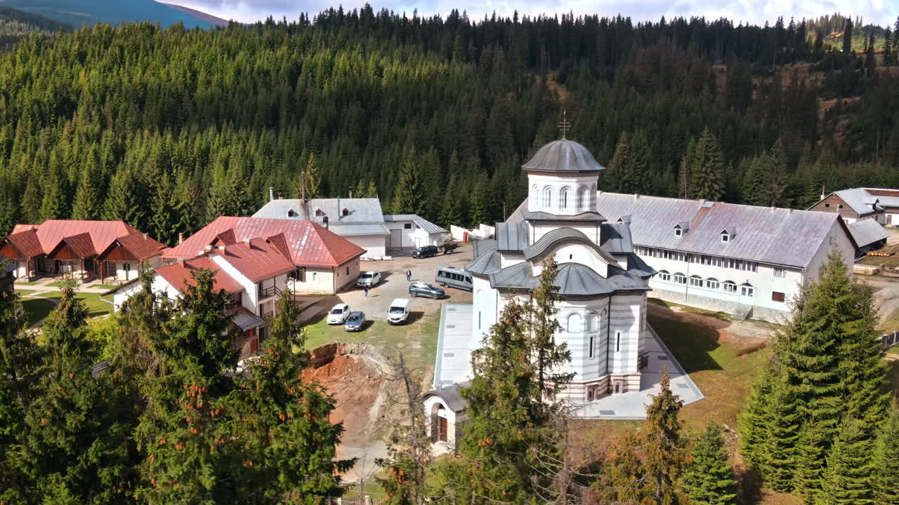 Aerial drone view of the Oasa Monastery in Romania. Churches, visitors, parked cars, carpathian mountains, hills covered with forest