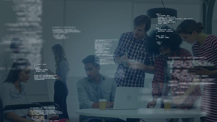 Seated engineer starting laptop, team leaning in at table reviewing app with floating code overlay