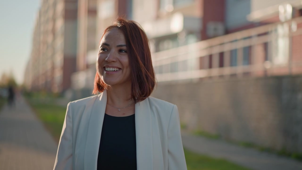 Jovem mulher caminhando por uma rua residencial sob a luz quente da tarde, exibindo postura relaxada, movimento sutil do cabelo e um sorriso e foco em mudança, transmitindo uma energia de estilo de vida natural.